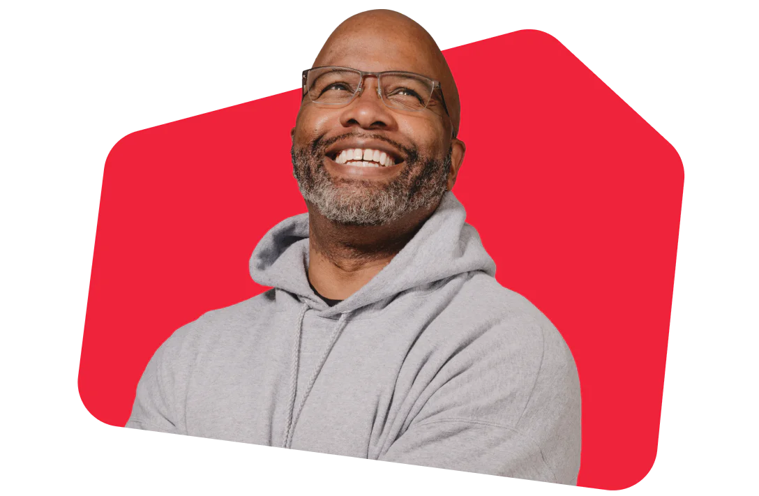 Man with glasses and gray hoodie smiling in front of a red background