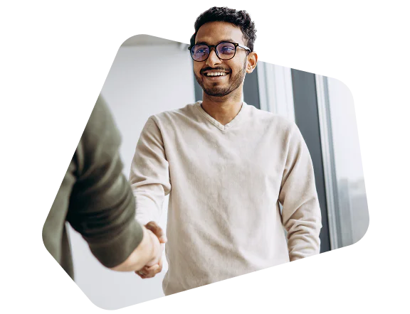 Smiling man in glasses shaking hands with another person in an office setting.
