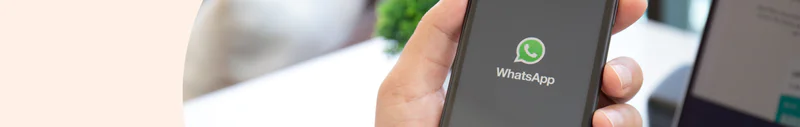 Hand holding smartphone displaying WhatsApp logo on the screen