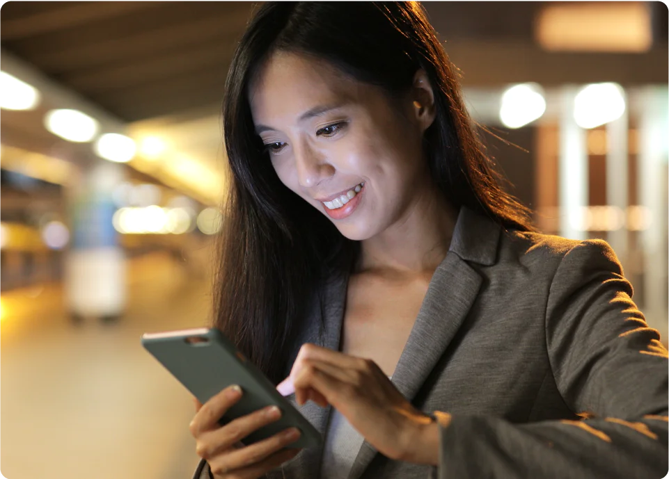 Businesswoman smiling while using a smartphone in a modern, well-lit environment.