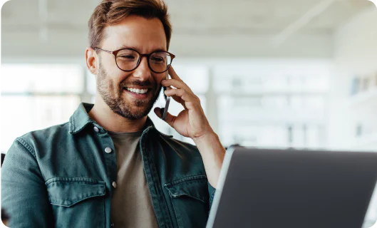 Smiling man with glasses talking on the phone and using a laptop