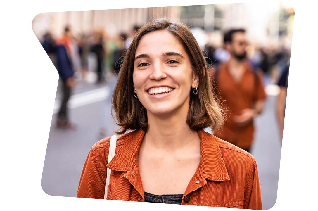 Woman with brown hair and a nose ring smiles while standing outside at a busy event.