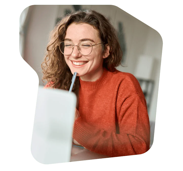 Woman in an orange sweater smiling while looking at a laptop screen.