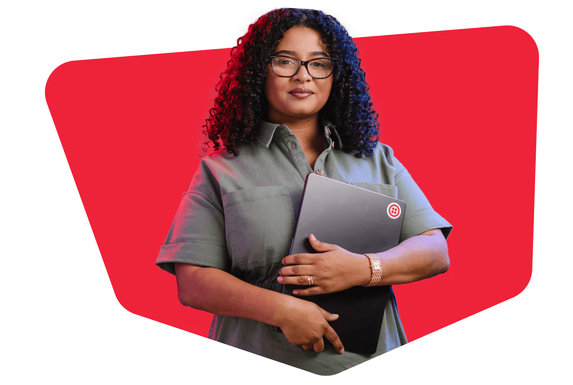 Woman with curly hair and glasses holding a laptop against a red background