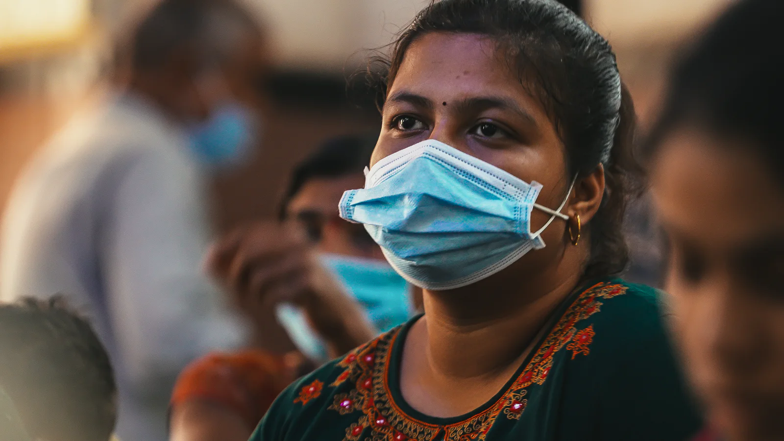 Woman wearing a face mask stands out in a crowd, looking ahead with a thoughtful expression.