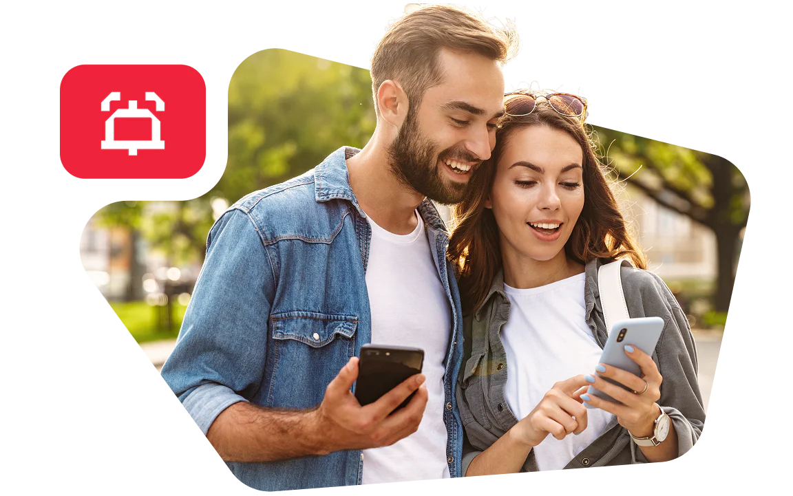 Smiling couple looking at their smartphones while standing outside.